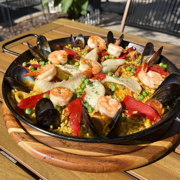 A large paella pan filled with seafood paella, featuring mussels, shrimp, fish, red peppers, and peas.
