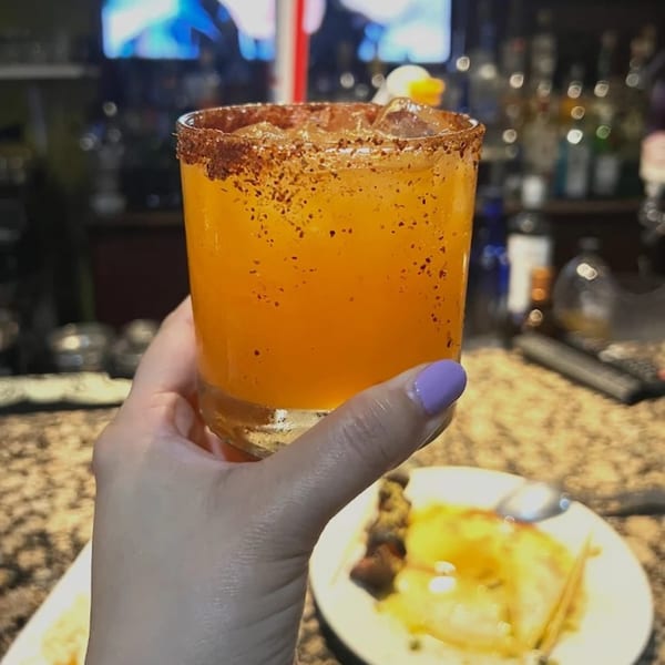 A hand holding a Guardado's Restaurant Spanish cocktail with a chili-salted rim and ice.